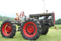 a little boy sitting on the front of a tractor in a field with red rims