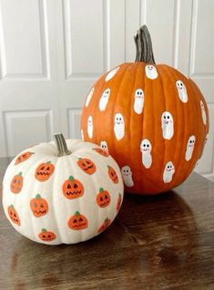 two pumpkins with ghost faces painted on them sitting on a table next to each other