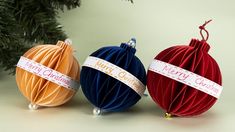 three christmas balls with ribbons on them sitting next to a tree