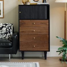 a black and brown chest of drawers next to a chair in a room with pictures on the wall