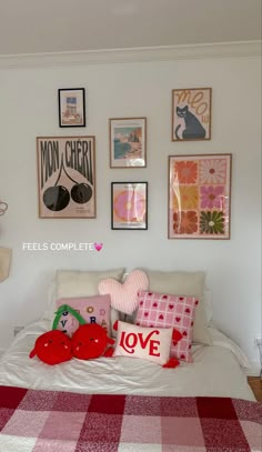 a white bed topped with lots of pillows next to pictures on the wall above it