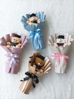 four small teddy bears wrapped in paper and tied with ribbons, sitting on a white surface