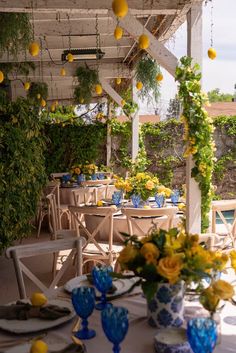 an outdoor dining area with blue and white vases filled with yellow flowers on the table