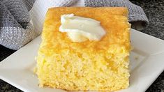 a piece of cornbread cake with cream on top sitting on a square white plate