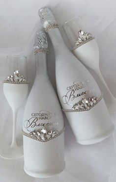 three white wine bottles with silver embellishments and two champagne flutes on a white background