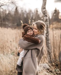 a woman holding a baby in her arms while standing next to a tree and grass