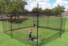 two young boys are playing baseball in a batting cage on the grass, and one boy is holding a bat