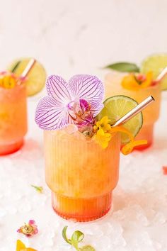 three glasses filled with drinks and garnished with flowers, limes and orange slices