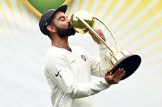 a man with a beard holding a trophy and kissing it in front of a backdrop