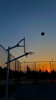 a basketball hoop and net at sunset with the sun setting in the distance behind it