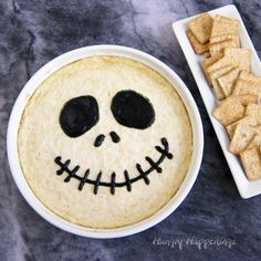 a bowl of crackers with a skull face painted on it next to a plate of cookies