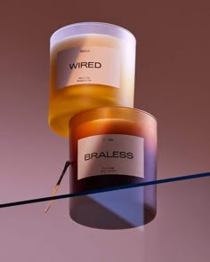 two candles sitting next to each other on top of a glass table and one candle has the word wired written on it