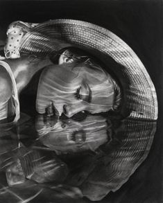 a black and white photo of a woman in a hat with her reflection on the water