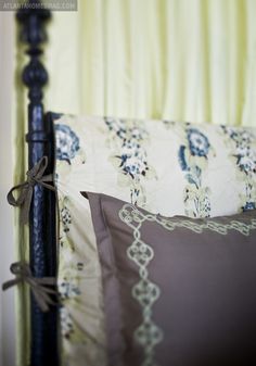 a bed with two pillows on it and a black headboard in front of a yellow curtain