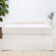 a bed with white sheets and pillows in a room next to a potted plant