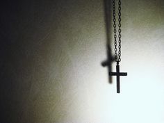 a black cross hanging from a chain on a wall in a dark room with light coming through the window