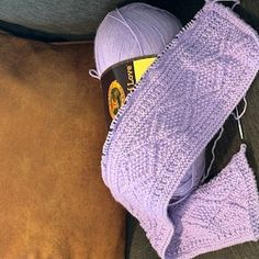 a purple crochet bag sitting on top of a couch next to a ball of yarn