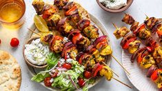 two plates with skewered meat and vegetables on them next to pita bread