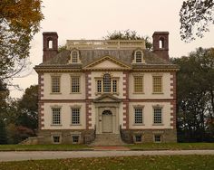 an old brick house with two chimneys on the top and second story, in front of some trees