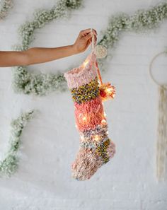 a person holding a christmas stocking with lights on it in front of a white brick wall