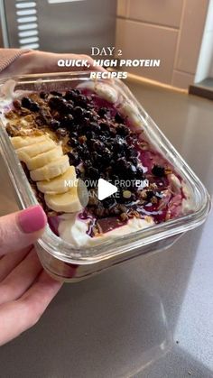 a person holding up a container of ice cream with bananas and blueberries in it