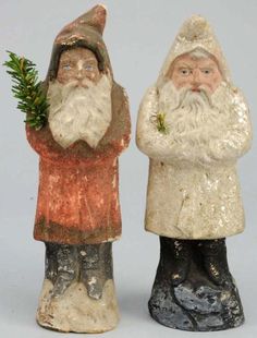 two small statues of santa claus holding a plant