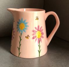 a pink pitcher with colorful flowers painted on it's side and bees flying around