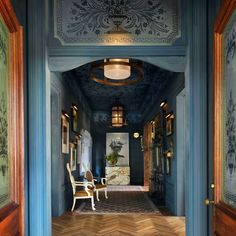 an ornate hallway with blue walls and wood flooring, two chairs on the far side