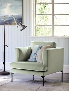 a light green chair sitting in front of a window with a lamp on top of it