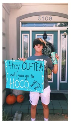 a boy holding a sign that says hey cutea will you go to hoco with me?