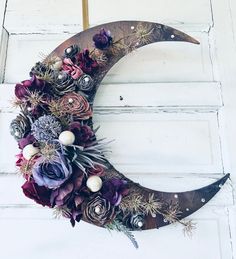 a crescent decorated with purple flowers and succulents is hanging on a door