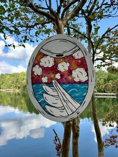 a sign hanging from the side of a tree next to a body of water with clouds in it