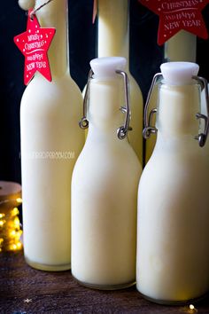 three glass milk bottles sitting next to each other on top of a wooden table with christmas lights in the background