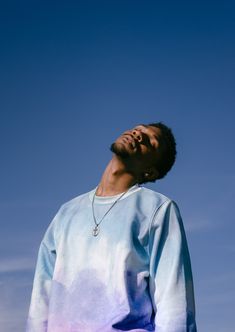 a man with his eyes closed wearing a tie dye shirt and necklace looking up into the sky