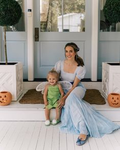 a woman sitting on the steps with a baby in her lap and pumpkins behind her