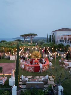 an outdoor seating area with candles lit up in the background and people standing around it