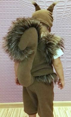 a small child wearing a costume with fur on it's head and ears, standing in front of a wall