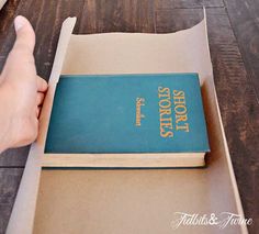 a person is holding a book in their hand while sitting at a table with a laptop