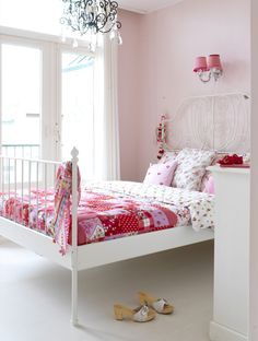 a white bed sitting next to a window in a room with pink walls and furniture