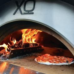 two pizzas sitting in front of an oven with fire coming from the top and bottom