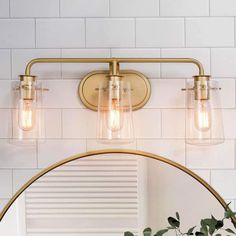 a bathroom vanity light with three lights and a round mirror on the wall above it