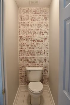 a white toilet sitting inside of a bathroom next to a wall with bricks on it