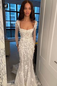 a woman in a white wedding dress standing in front of a mirror with her hands on her hips