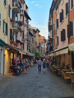 people are walking down the street in an old european town with shops and restaurants on both sides