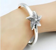 Enhance your jewelry collection with our exquisite Dotted Starfish Bangle, expertly crafted from 925 Sterling Silver. This elegant spring-hinged bracelet combines both style and comfort in a lightweight design that's easy to wear. With an inside circumference of 6.5 inches (16.5 cm), it provides a comfortable fit for most wrists. Each bangle is stamped with '925' to assure you of its sterling silver authenticity. The hollow construction allows for a bold look without the added weight, making it Silver Starfish Bracelet For Gift, Silver Starfish Bracelet, Adjustable Silver Starfish Jewelry, Hinged Bracelet, Beach Jewelry, Starfish, Bangle Bracelets, Jewelry Collection, Jewelry Bracelets