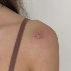 the back of a woman's shoulder with a small sun tattoo on it