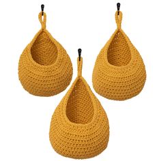 three yellow crocheted baskets hanging from hooks on a white background with black handles