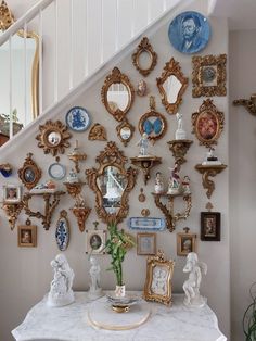 there is a wall with many different pictures and mirrors on it, along with a vase filled with flowers