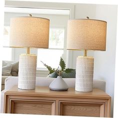 two white vases sitting on top of a wooden table next to a lamp and mirror