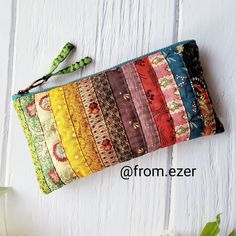 a multicolored zipper pouch sitting on top of a white wooden table next to flowers